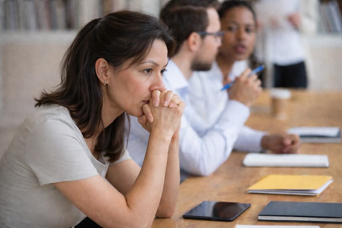 Female executive sitting nervously in a meeting, looking tense and silent in thought while others speak