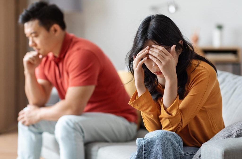 couple sitting apart in tension at home showing emotional stress and communication breakdown, which can be worked on through relationship coaching