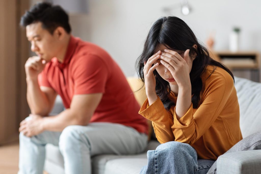 couple sitting apart in tension at home showing emotional stress and communication breakdown, which can be worked on through relationship coaching