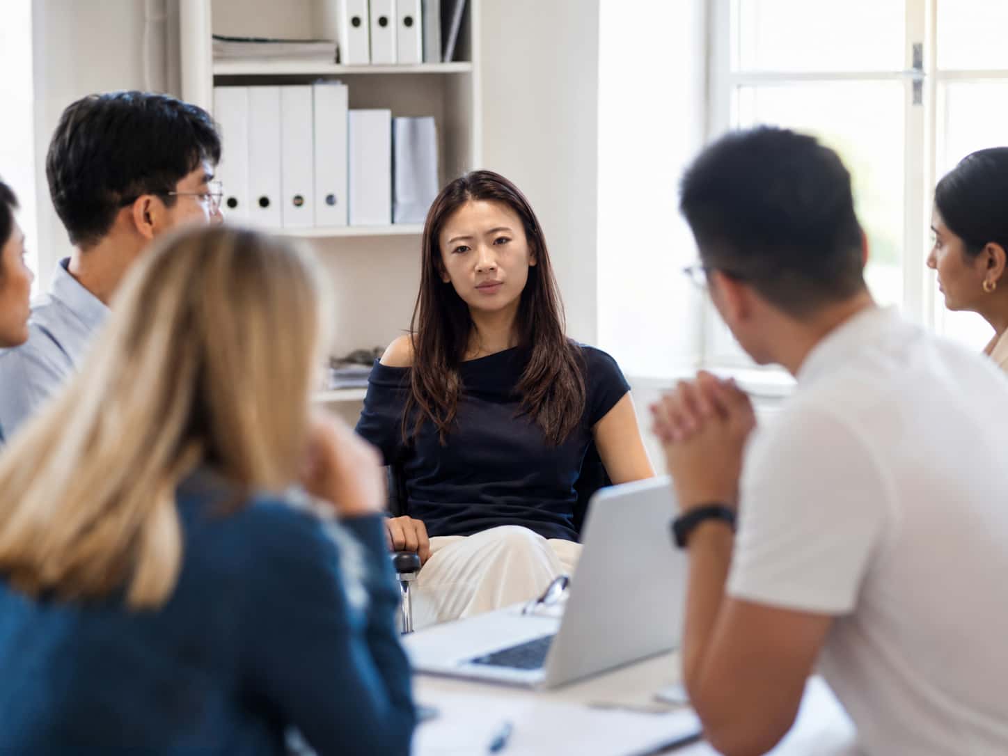 Young professional woman at the centre of a small group meeting, navigating the pressure of being heard — the core territory of ontological coaching.