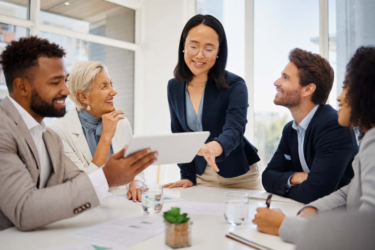 Young professional woman leading a diverse executive team meeting with confidence, demonstrating advanced public speaking skills in an interpersonal setting.